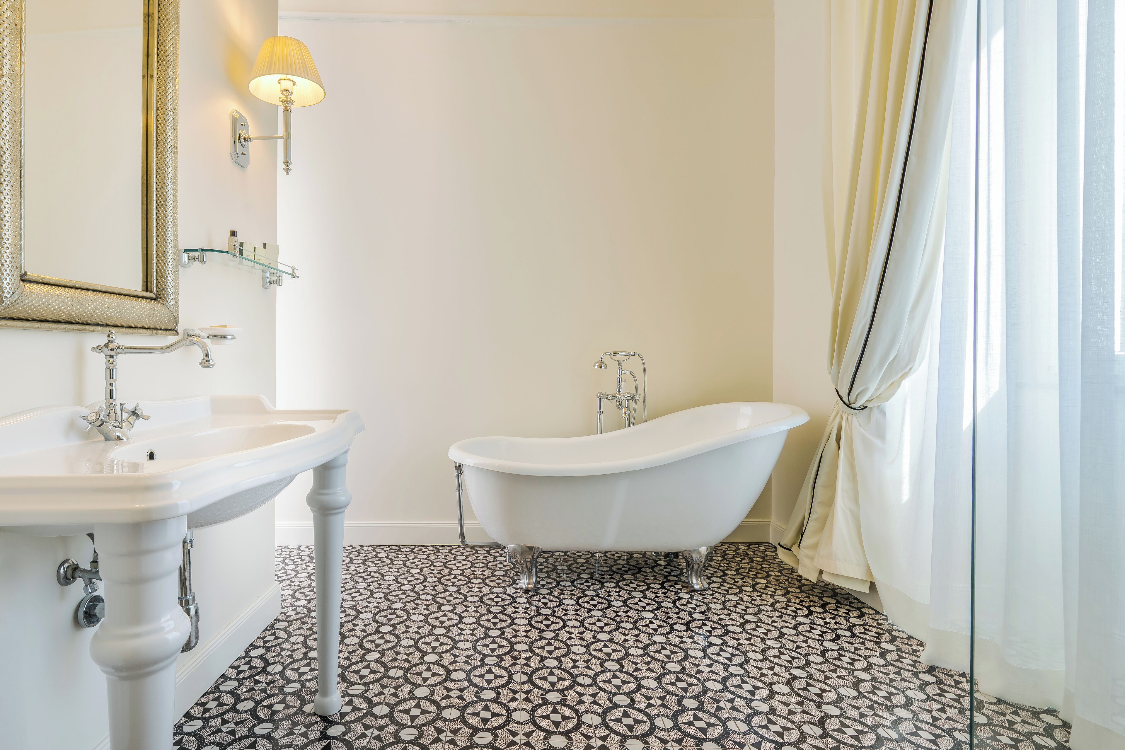 Une salle de bain avec une baignoire sur pieds, un lavabo sur colonne et un miroir fixé au mur.