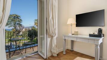 Een kamer met balkon, een tafel met stoelen, een bureau met lamp en een flatscreen televisie.