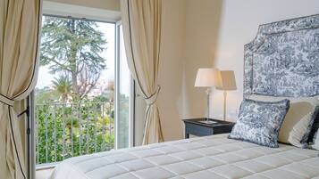 A bedroom with a large bed, a nightstand with a lamp, and a view of greenery outside.
