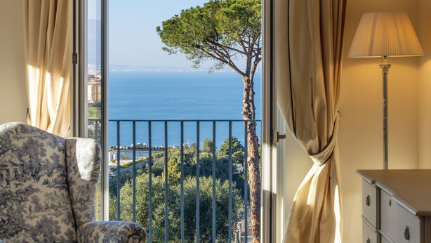Una habitación con vista al mar, una silla, un aparador y cortinas.