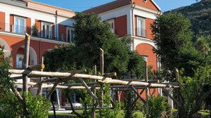 Un edificio con fachada roja, balcones y una pérgola de madera al frente.