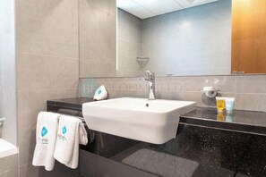 Une salle de bain moderne avec un lavabo blanc, un plan de toilette foncé et un grand miroir.