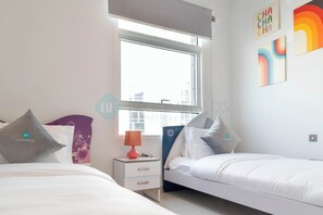 A bedroom with two beds, a window, and artwork on the wall.