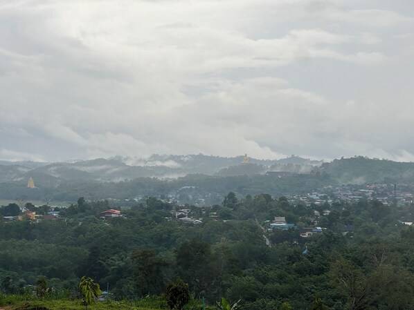 A mountainous landscape with a large golden statue on a hill, surrounded by dense greenery and scattered buildings. - phetruntee resort (Sangkhla Buri)