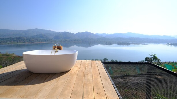 A large white bathtub on a wooden deck overlooking a calm lake with mountains in the distance. - phetruntee resort (Sangkhla Buri)