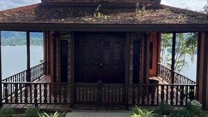 A traditional wooden building with a steeply pitched roof, a central entrance with double doors, and a balcony with a railing. - phetruntee resort (Sangkhla Buri)