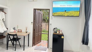 A room with a TV displaying a beach scene, a small fridge, a table with a chair, and a door leading outside. - phetruntee resort (Sangkhla Buri)