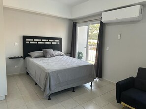 Relax in a spacious bedroom with a large bed, black headboard, and grey bedspread, surrounded by a clean, minimalist design.