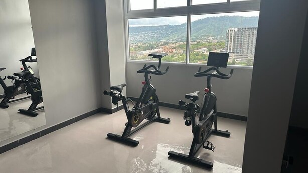 Une salle de sport équipée de deux vélos d’appartement, d’un grand miroir et offrant une vue sur le paysage urbain par une fenêtre.