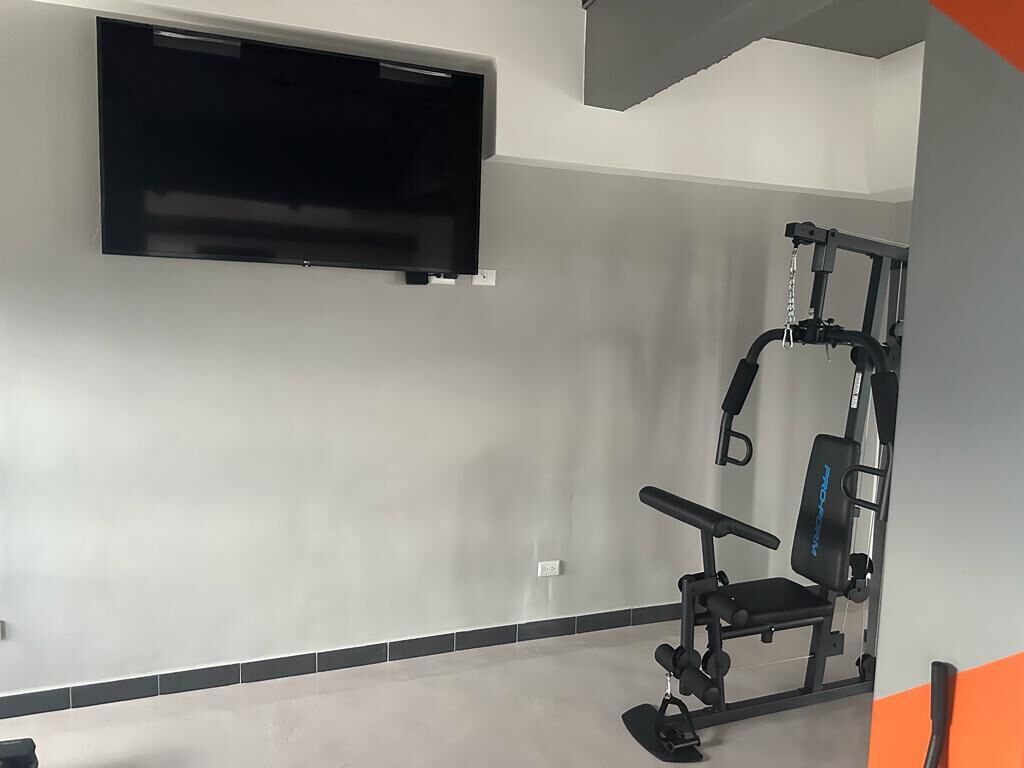 Ein Fitnessraum mit Wandfernseher, einer Bank und einem Kraftgerät.