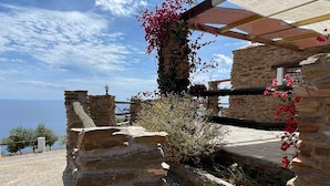 Una struttura in pietra con una pergola, vista sul mare e piante fiorite.