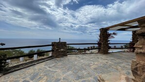 Una terrazza in pietra con vista sul mare, caratterizzata da colonne in pietra e un pergolato in legno.