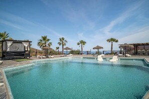 A clear blue pool with white lounge chairs and palm trees in the background.