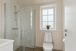Ein Badezimmer mit Duschkabine aus Glas, Toilette und Fenster mit Blumentopf.