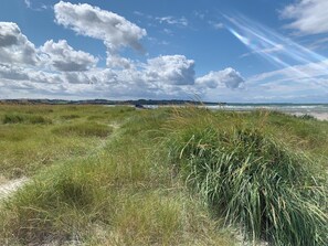 Eine Küstenlandschaft mit grasbewachsenen Dünen, einem Boot und einem weiten Blick auf das Meer unter einem bewölkten Himmel.