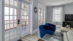 Ein Wohnzimmer mit einem Glastisch, einem blauen Sessel, einem weißen Sofa und einem Fernseher auf einem Lowboard.