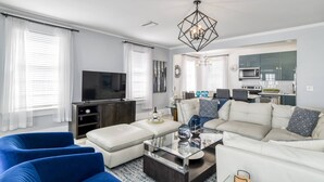 Ein modernes Wohnzimmer mit Flachbildfernseher, Glastisch und blauen und weißen Möbeln.