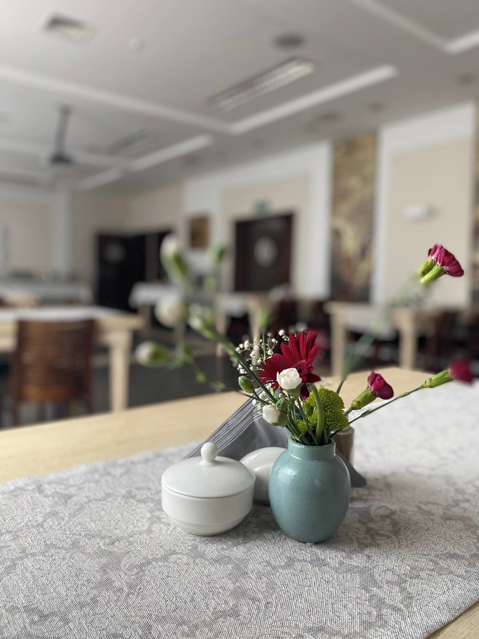 Una sala moderna con comedor al fondo, con un jarrón de flores sobre una mesa.
