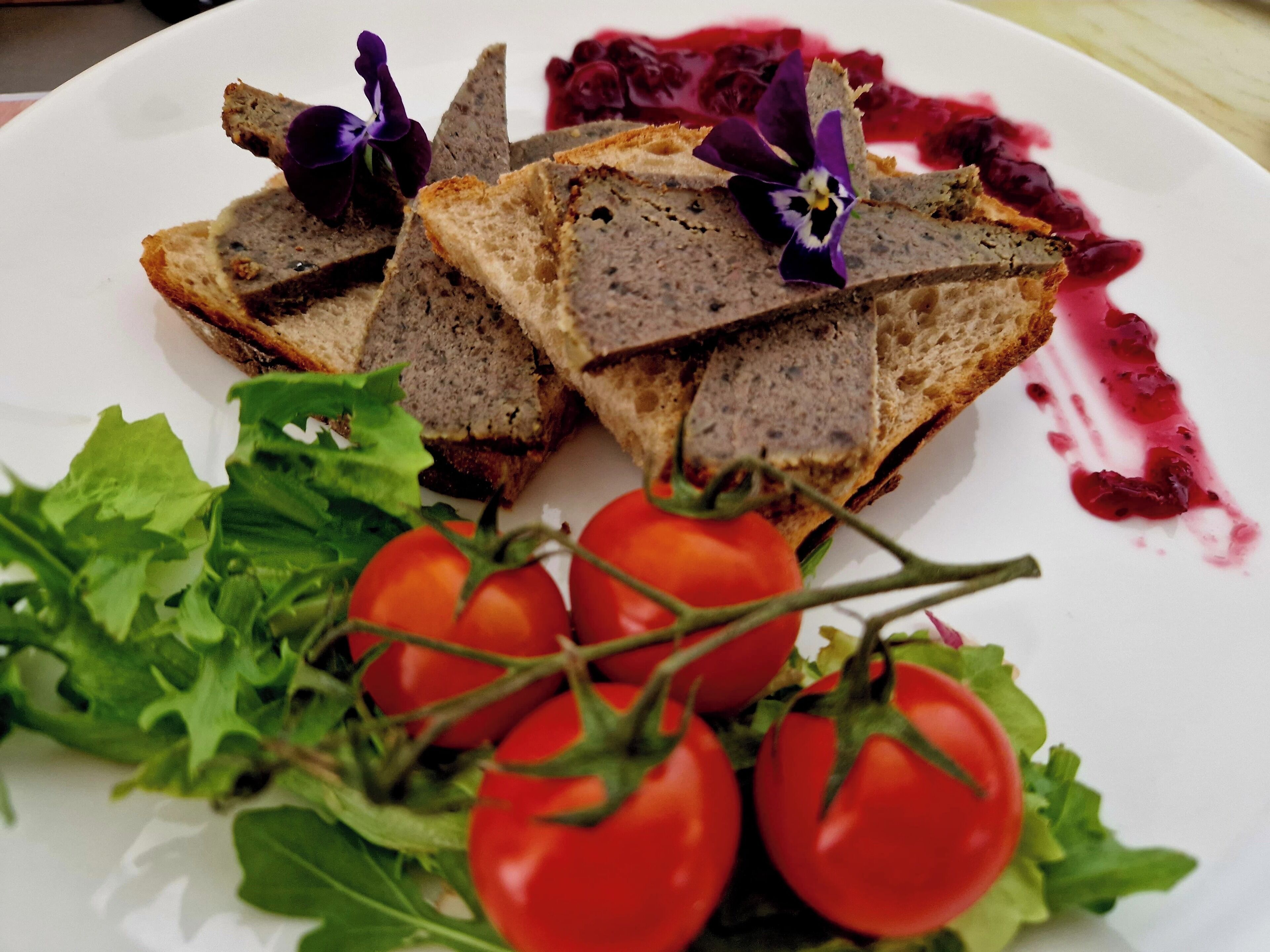 A plate with sliced bread topped with a dark spread, surrounded by cherry tomatoes and a small purple flower.