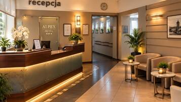 Uma área de recepção de hotel com balcão, relógio e espaço de espera com mesas e cadeiras.