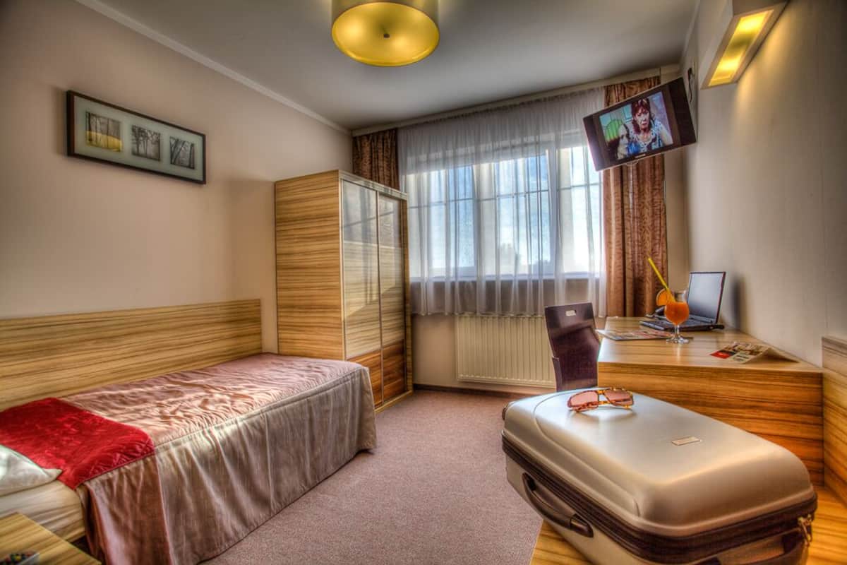 A hotel room with a bed, a desk with a laptop, a television, and a suitcase.