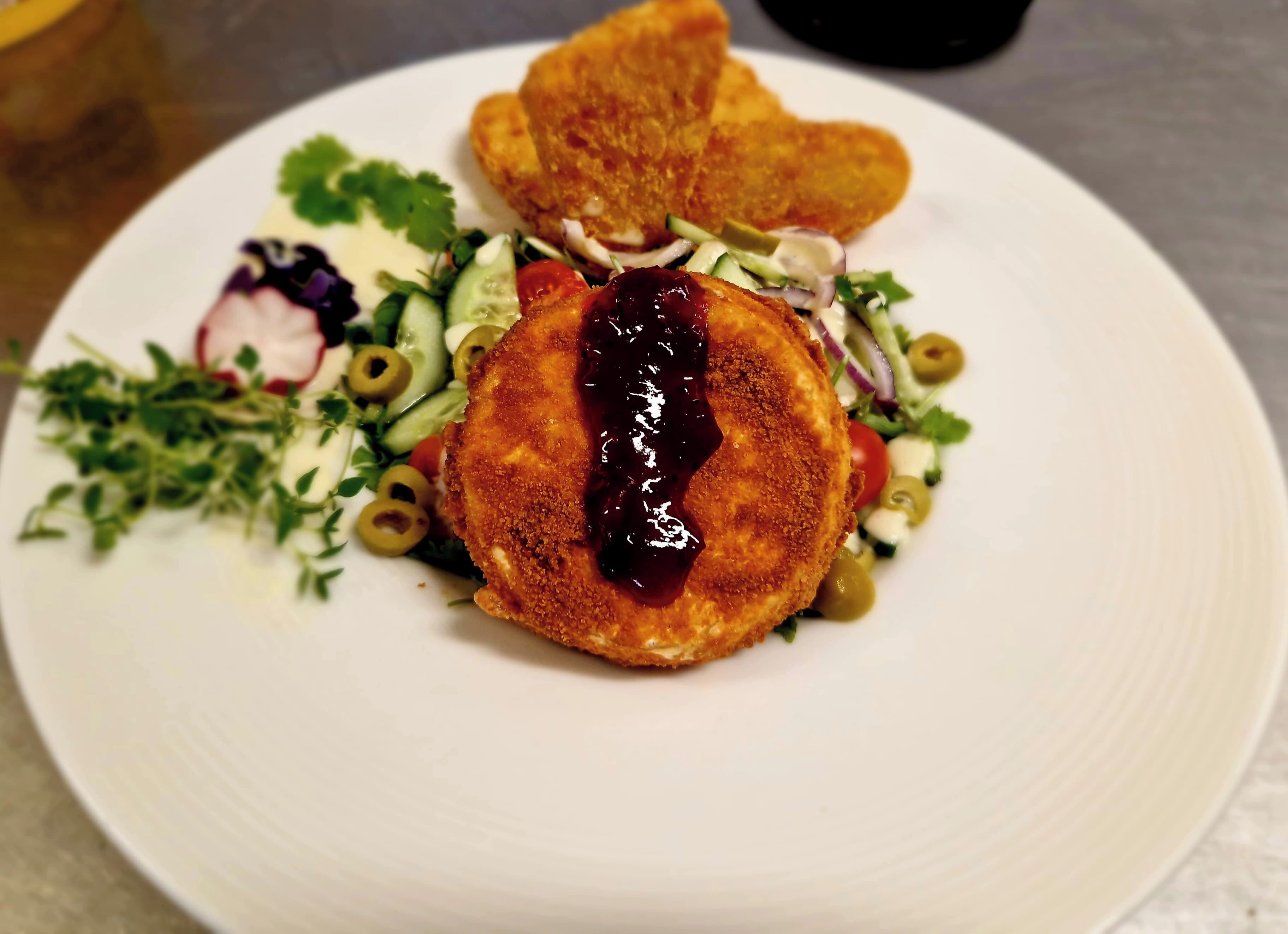 A plate with a breaded item, salad, and a small bowl of sauce.