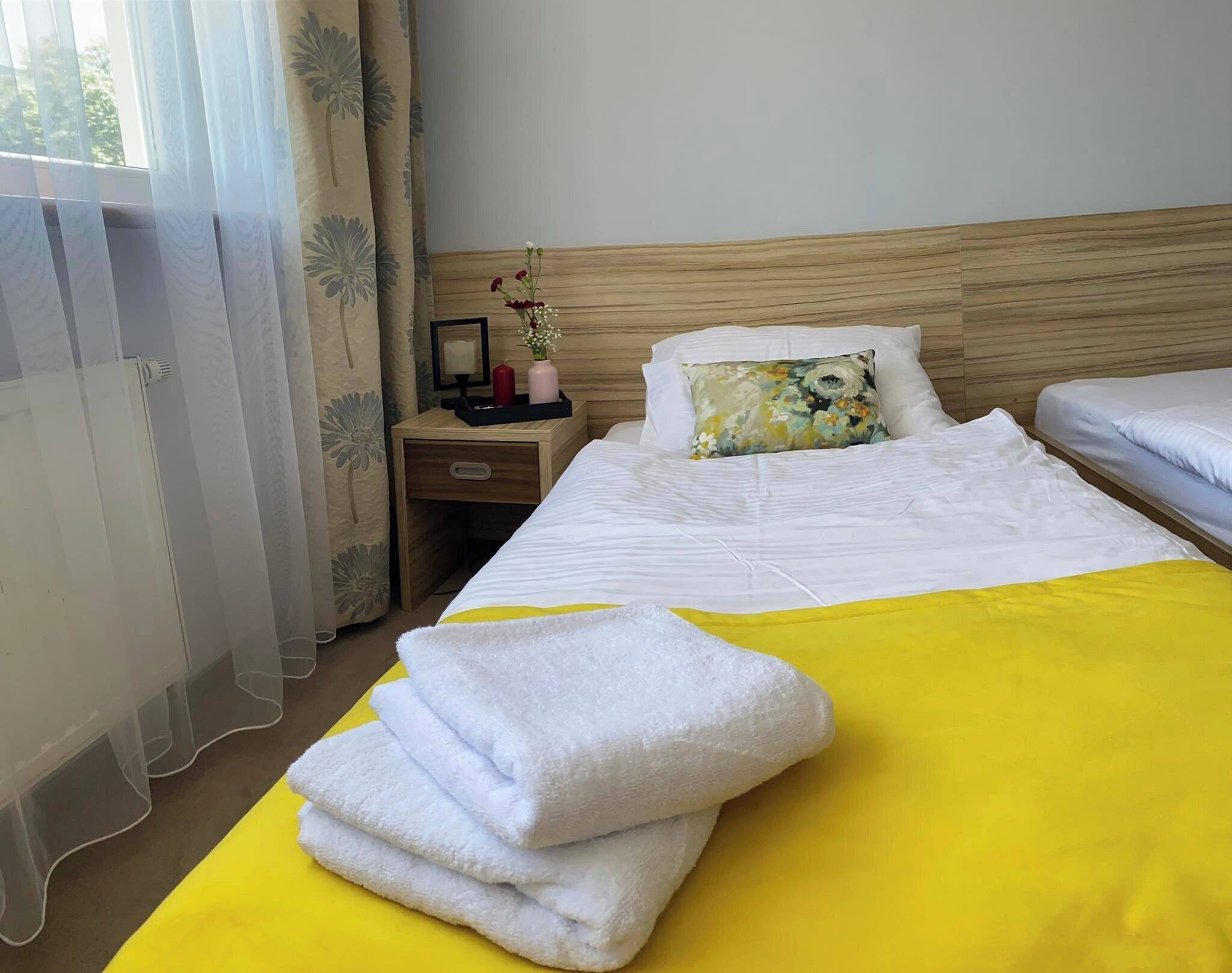 Una habitación de hotel con cama, mesita de noche, espejo y ventana con cortinas.