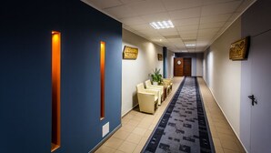 A hotel reception area with a reception desk, seating area, and a carpeted hallway. - Hotel Alpex  (Zabrze)