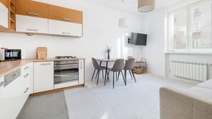 A modern kitchen with white cabinets, a wooden countertop, and a dining area with a table and chairs. - RentPlanet - Apartament Śniadeckich (Warsaw)