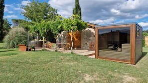 Un patio exterior moderno con pared de piedra, terraza de madera y una estructura de vidrio.