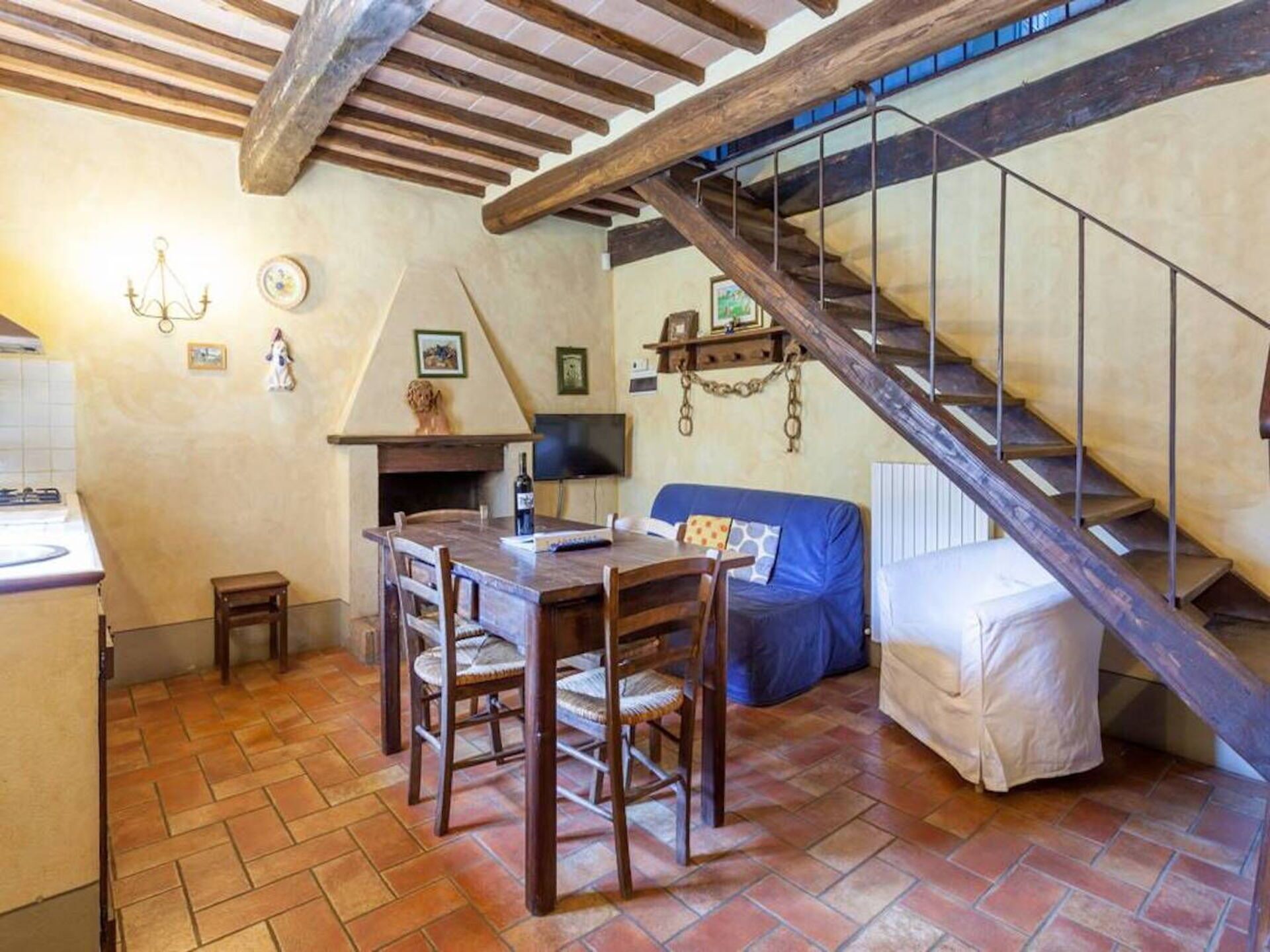 Un intérieur rustique avec une table à manger en bois, des chaises, un canapé et un escalier doté d’une rampe en métal.
