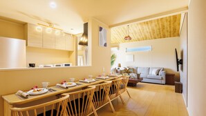 A modern dining area with a long wooden table, multiple chairs, and a sofa in the background. - Yanbaru villa -KISEN- (Motobu)