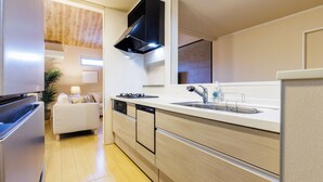 A modern kitchen with a built-in stove, dishwasher, and sink. There is a small seating area with a couch and a plant. - Yanbaru villa -KISEN- (Motobu)