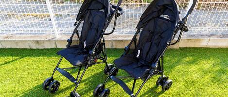Two strollers parked on a grassy area with a white fence in the background.