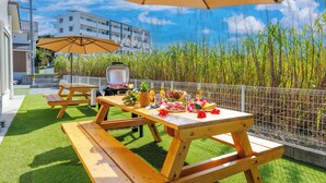 An outdoor patio with a wooden table set for a meal, a grill, and a large umbrella providing shade. - Yanbaru villa -KISEN- (Motobu)