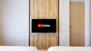 A hotel room with a bed, a wooden panel wall, and a television mounted above the bed displaying the YouTube logo. - Yanbaru villa -KISEN- (Motobu)