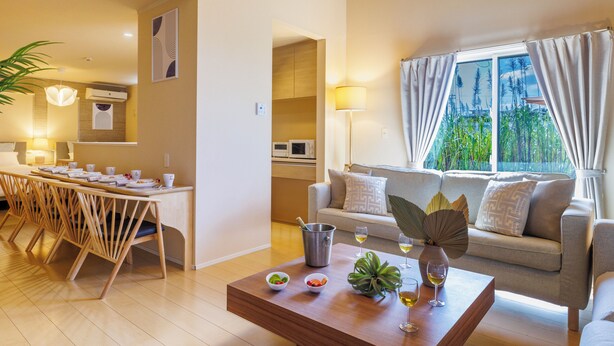 A modern living room with a sofa, a dining table with chairs, a coffee table, and a view of greenery through the window. - Yanbaru villa -KISEN- (Motobu)