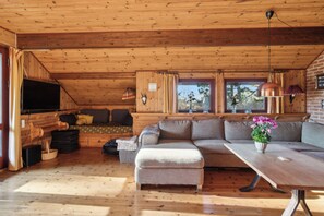 Interior acolhedor de uma cabana com teto de madeira, sofá seccional, mesa de jantar e televisão.
