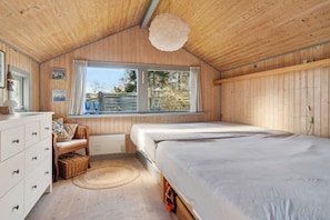 Een kamer met houten lambrisering, een groot bed, een dressoir, een stoel en een raam met gordijnen.