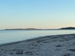 Een strand met een heldere lucht, rustig water en heuvels in de verte.