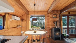 Un interior de madera con una mesa redonda para comer, una estufa empotrada y vistas a través de un ventanal.