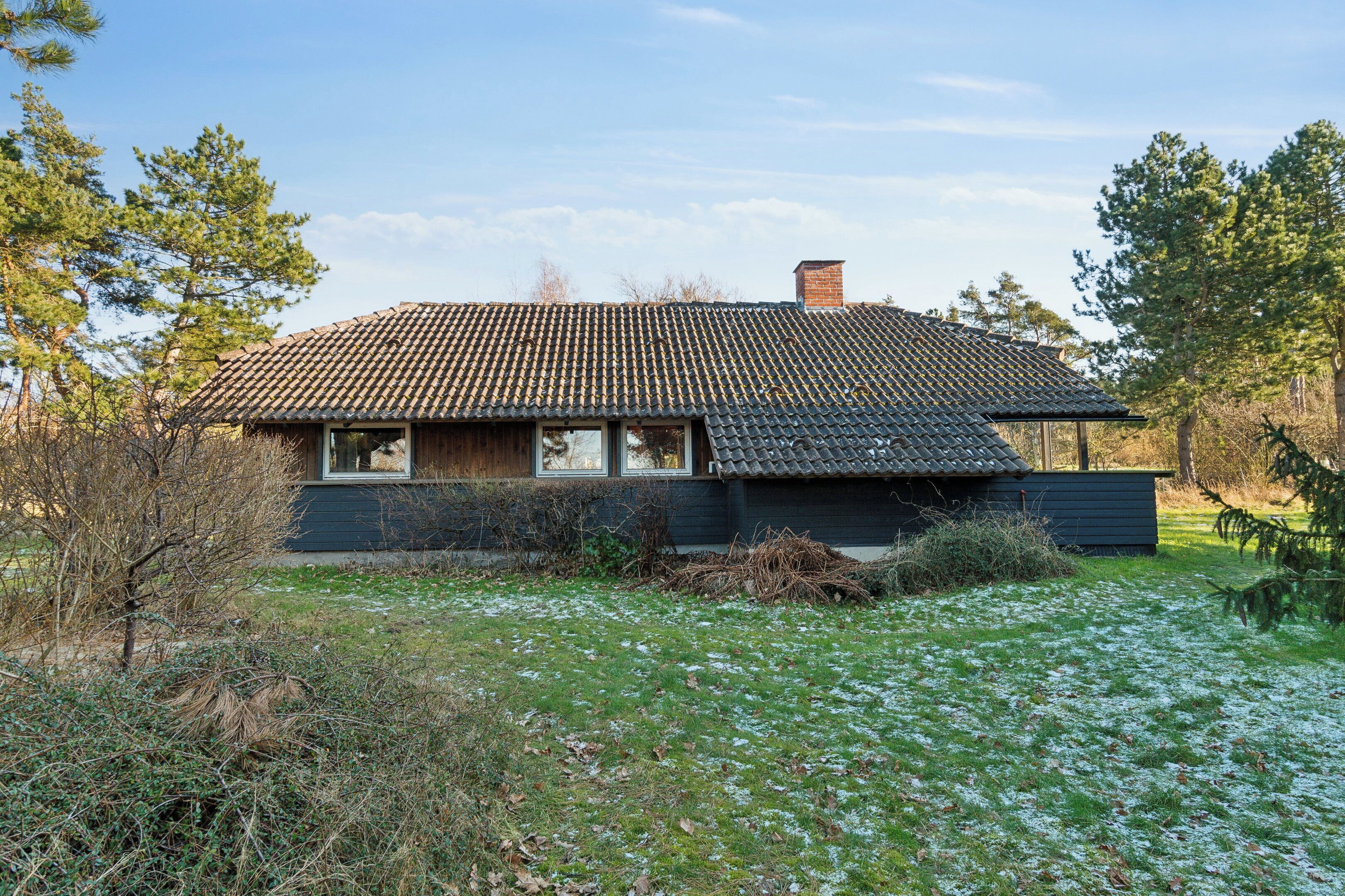 A house with a tiled roof, a chimney, and a front yard with grass and bushes.