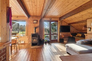 Interior acolhedor de uma cabana com lareira, piso de madeira, sofá e área de refeições.