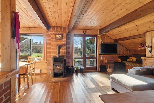 Een gezellig houten interieur met een open haard, houten vloeren, een bank en een eethoek.
