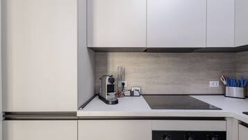 A modern kitchen with white cabinets, a built-in stove, and a coffee machine.