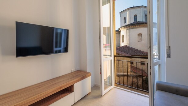 A modern apartment with a flat-screen TV mounted on the wall, a wooden bench, and a balcony with a view of buildings. - GuestHost - In the heart of Bergamo, a cozy 45 sqm apartment for 3 guests, located on the third floor with an elevator (not suitable for disabled persons). Its central location allows you to fully experience the city, with shops, restaurants, and service (Bergamo)
