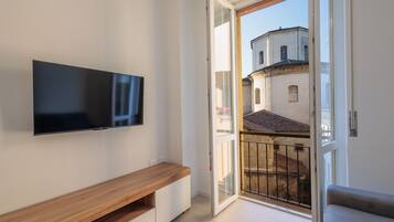 A modern apartment with a flat-screen TV mounted on the wall, a wooden bench, and a balcony with a view of buildings.