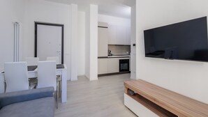 A modern living room with a flat-screen TV, a sofa, a dining table with chairs, and a kitchen area in the background. - GuestHost - In the heart of Bergamo, a cozy 45 sqm apartment for 3 guests, located on the third floor with an elevator (not suitable for disabled persons). Its central location allows you to fully experience the city, with shops, restaurants, and service (Bergamo)