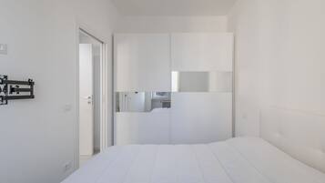A modern hotel room with a large bed, a wardrobe, and a small kitchenette area.
