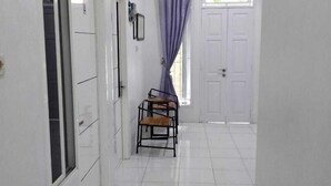 Un corridoio con pavimento piastrellato di bianco, una porta a sinistra, una sedia al centro e un'altra porta in fondo.